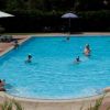 Piscina con bagnanti e ombrelloni, circondata da verde.