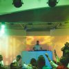 DJ su palco con pubblico in una discoteca illuminata.