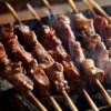 Spiedini di carne cotti alla griglia con fumo visibile.