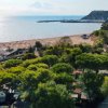 Una spiaggia con ombrelloni e un molo, circondata da alberi e una collina in lontananza.