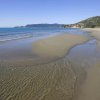 Spiaggia sabbiosa con onde leggere e colline sullo sfondo.