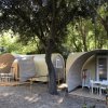 Due tende moderne in un'area boschiva con sedie e tavoli davanti.