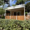 Un bungalow moderno con veranda e ringhiera in legno circondato da alberi e siepi verdi.