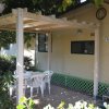 Veranda esterna con tavolo e sedie bianche, vicino a una casa beige.