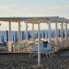 Tettoia bianca in spiaggia con sedie e ombrelloni blu.