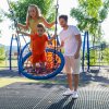 Due bambini su un'altalena a nido con un adulto in un parco giochi.