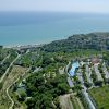 Vista aerea di un campeggio vicino alla costa, circondato da verde e colline.