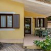Casetta gialla con porta e finestre aperte su patio ombreggiato.