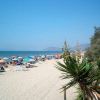 Una spiaggia affollata, con ombrelloni colorati e alberi sul lato.